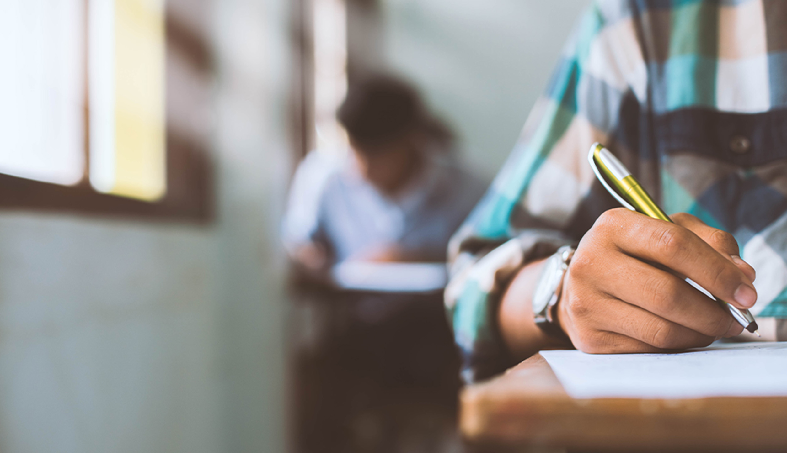 Students writing and reading exam sheets in classroom.